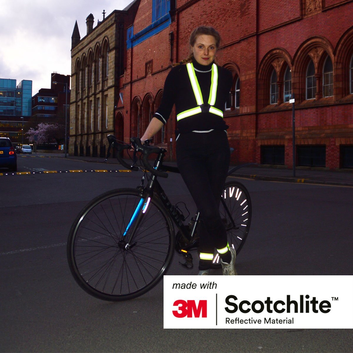 Smiling person stood next to a bike wearing the Yellow high vis cross belt